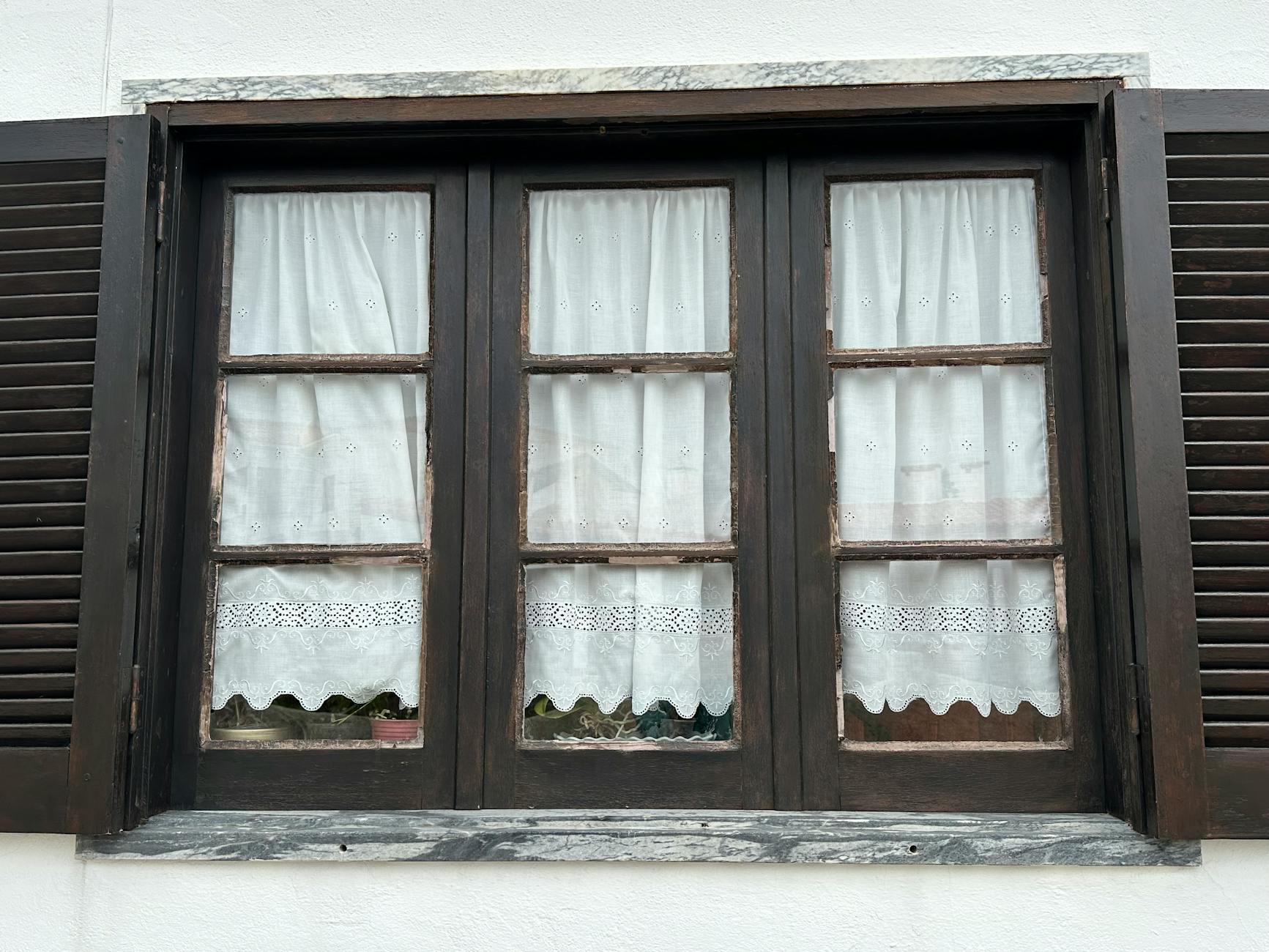 Stare drewniane okno z okiennicami i koronkową firanką w grubym murze