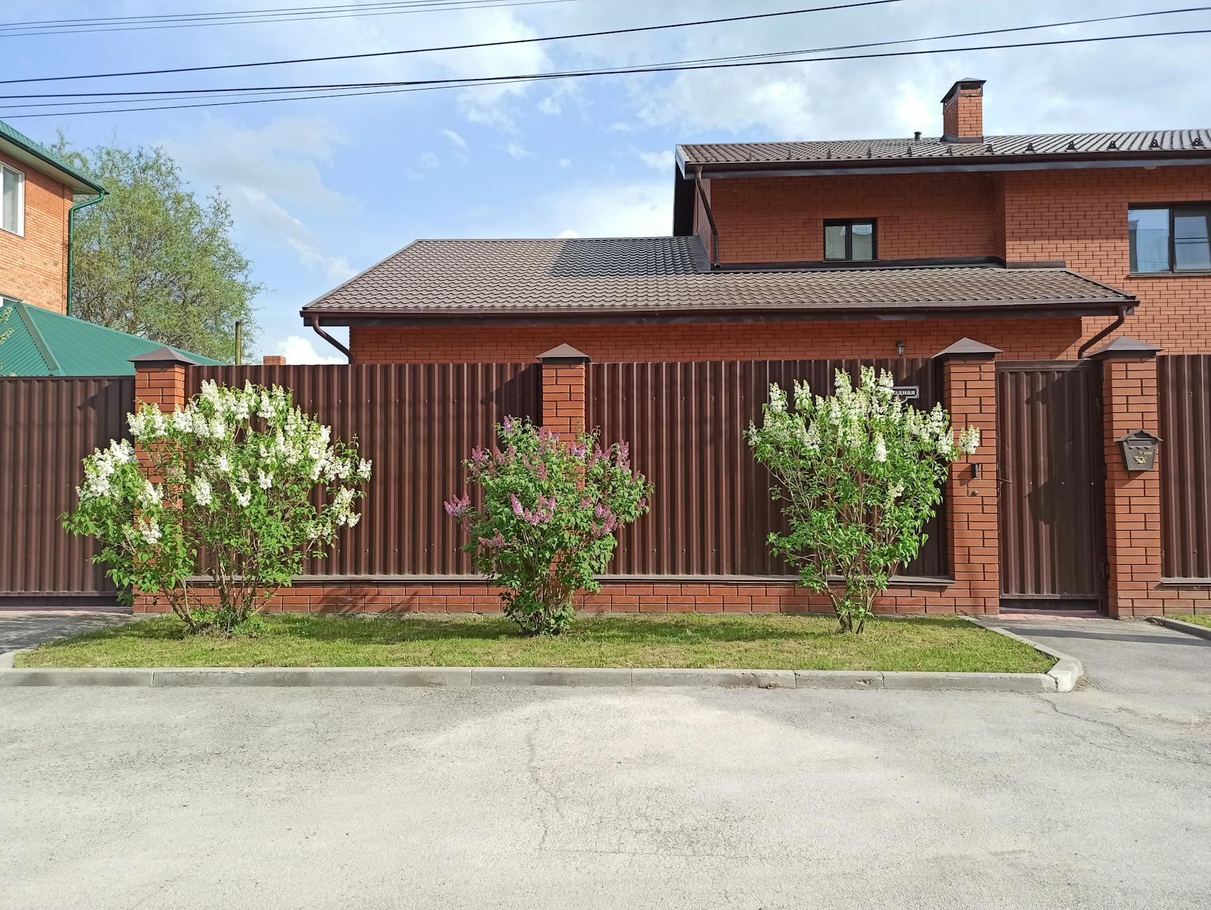 Nowoczesne ogrodzenie z brązowego metalu przy murowanym domu z ogrodem