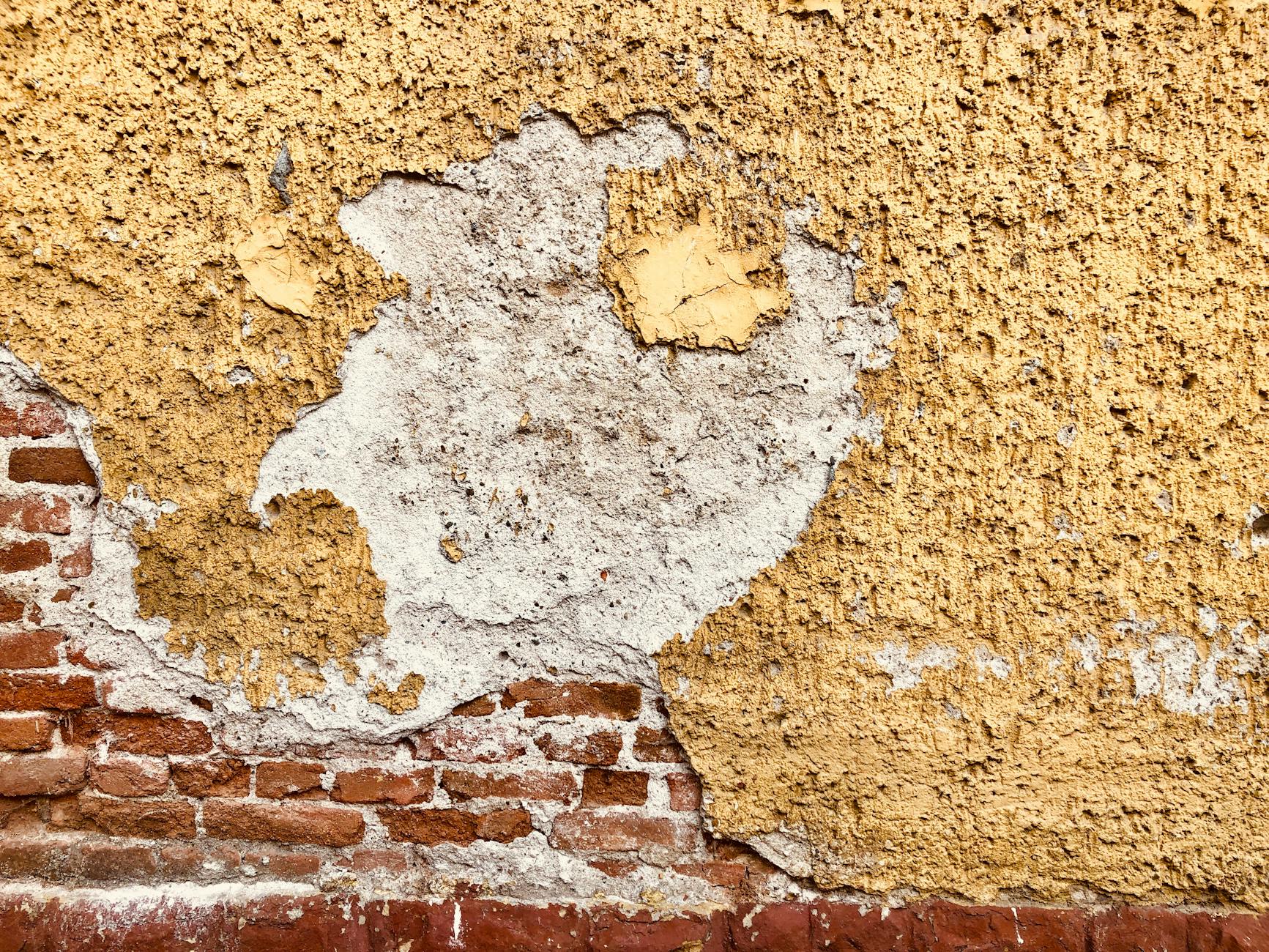 Zbliżenie zniszczonej ściany z odlatującym żółtym tynkiem i odsłoniętą cegłą