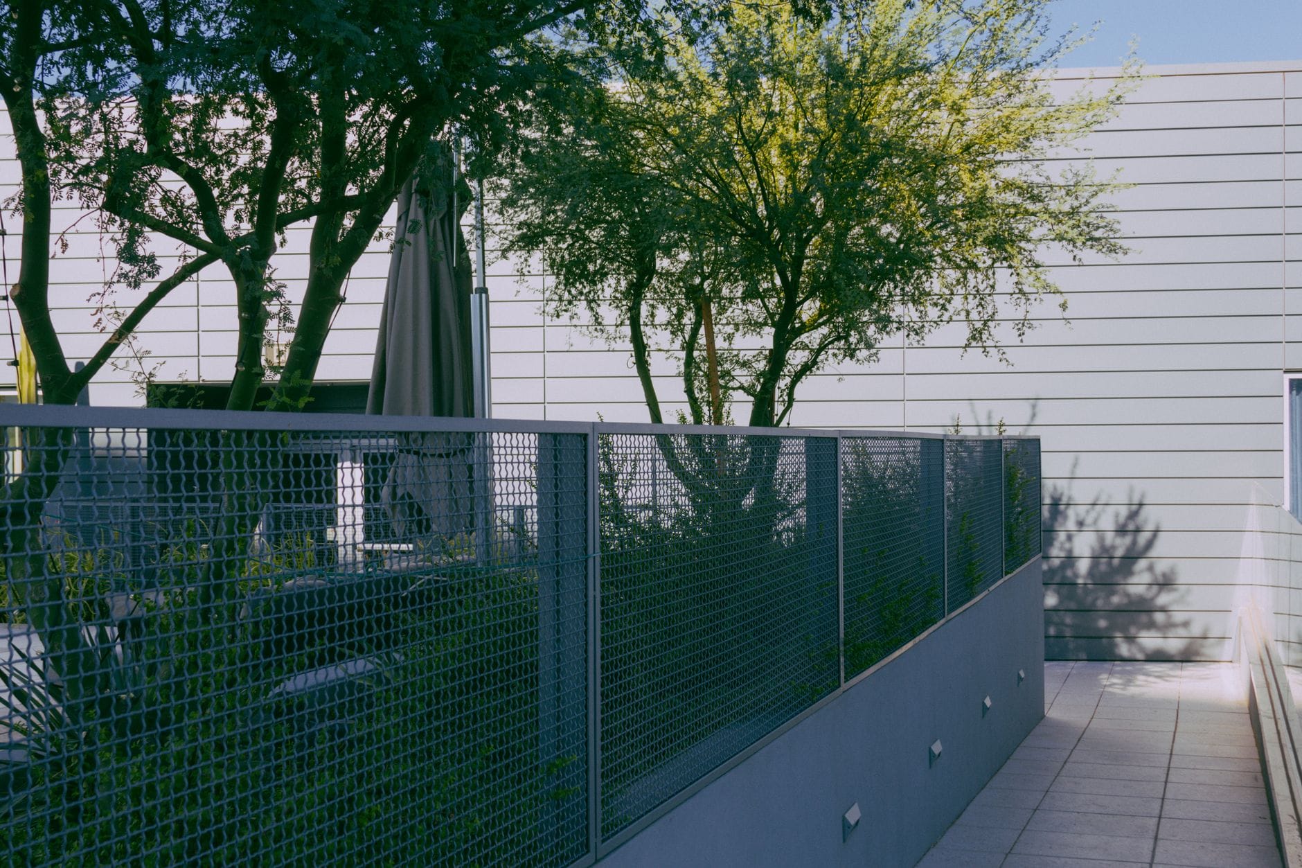 Nowoczesne patio w mieście z metalowym ogrodzeniem, drzewami i słońcem